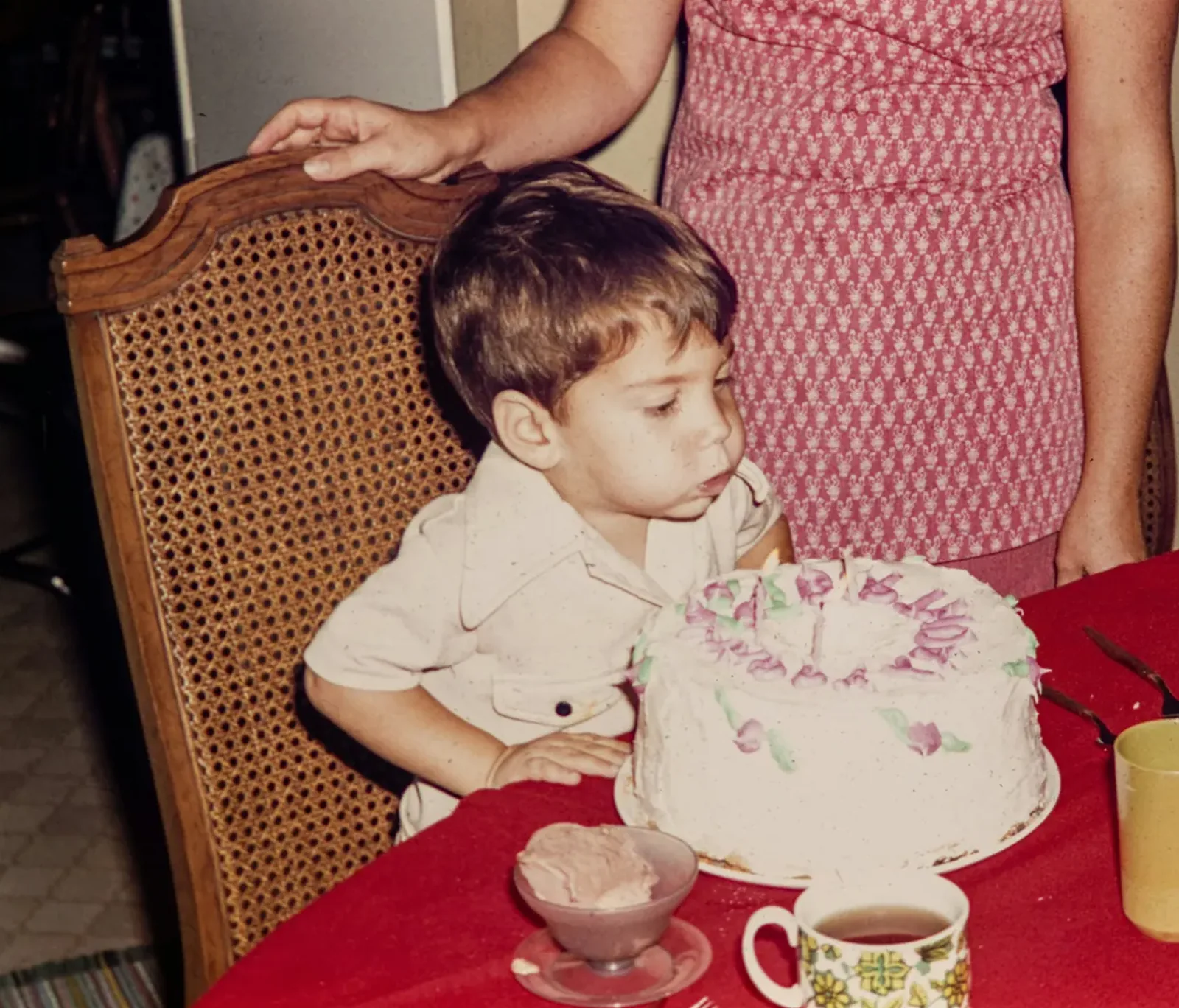 A vintage family photograph of a young boy about to blow out the candles on a birthday cake